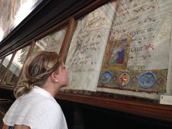 Students looks at illuminated manuscript under glass